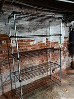 Overall angled view of metal shelving unit showing five wire mesh shelves and adjustable leg design.