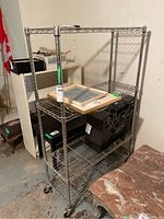 Front side view of the four tiered metal baker's style shelving unit showing wire shelves and casters.