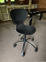 Front-left angled view of the black plastic office chair showing seat, backrest, metal base and casters