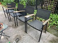 Four matching outdoor chairs with metal frames, black webbed backs and seats, and wooden armrests arranged on a patio.
