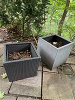 Photo of two large outdoor planters on a stone patio, surrounded by trees and foliage, showing the woven PVC and composite planter side by side with debris inside.