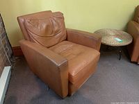 Brown leather armchair with cushioned back and seat displayed in a room with brick wall and green walls.