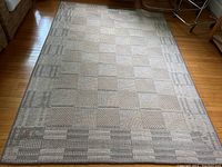 Full view of woven area rug on a hardwood floor, showing geometric pattern and overall condition.
