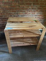 Two wooden storage shelves stacked or placed close, showing light-colored wood slat construction with visible screws in a brick-walled room.