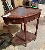 Full front and top angle view showing triangular table with two decorative drawers and a lower shelf, reddish wood tone finish showing some wear and dust.