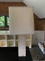 Front-facing photograph showing the tall rectangular textured stone base and the large square cream fabric shade with visible stitching.