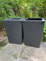 Two black woven poly planters standing outdoors on stone surface, showing overall shape and exterior condition.
