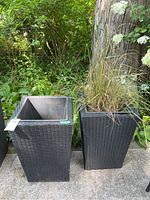 Two black tall tapered poly woven texture planters, one with dry grass, outdoors