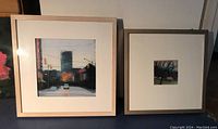 Photo showing both framed pastel artworks side by side, placed on grey surface with shadowed background