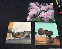 View of all three paintings on board showing different subjects: purple flowers, urban street with car, and landscape with trees.