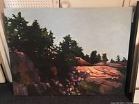 Front view of full oil painting on canvas showing rocky hillside and trees against sky