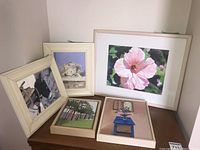 Photo of all five framed artworks together, showing variations in size and subject matter including flower, trees, still life, and sheep.