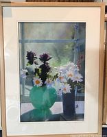Full view of framed pastel artwork showing flower still life with daisies and purple flowers in green and blue vases, signed T. Daniels, with visible mat and simple light wood frame.