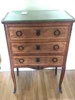Front view of three-drawer cabinet showcasing marquetry pattern on drawer fronts, brass ring pulls and central escutcheons