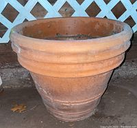 Side view of large terracotta clay planter, showing wide rim and tapered body with decorative horizontal ridges.