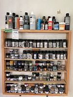 Wooden shelves filled with multiple jars and bottles of model paints and primers of various sizes and brands