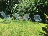 Four green wire mesh chairs arranged on lawn with shrubs in background