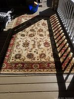 Full view of the rug on a porch showing floral design and border in neutral colors.