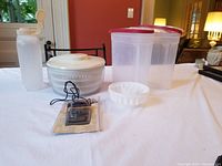 Full lot displayed on table: salad spinner, storage containers, jello mold, meat thermometer in packaging, large beverage container.