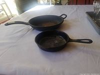 Two cast iron frying pans side by side on white cloth; one noticeably smaller than the other