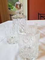 Crystal whiskey decanter and three matching glasses displayed on a white tablecloth with a red wall background.