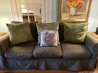 Photo showing three large green textured cushions and one smaller floral embroidered cushion on a grayish sofa