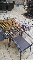 Photo of approximately 15 fishing rods with various handles and reels placed on outdoor glass table.