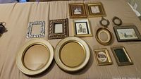 Twelve vintage frames laid out on beige fabric; includes various shapes and sizes, some with artwork and others empty.