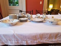 Full view of the Limoges set arranged on a table showing covered vegetable dish, open vegetable dish, dinner plates, cups and saucers, salad plates, creamer with saucer, and bowls all decorated with floral patterns and gold accents.