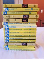 Stacked view of 15 Nancy Drew books showing yellow spines and titles with Carolyn Keene author credit.