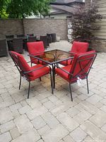 Full view of the patio table set with four red cushioned chairs on a stone patio with a brick wall background