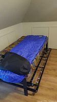 Blue sleeping bag laid out on a bed frame showing full length and black carrying case at foot end.