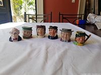 Photo showing the full set of 5 small toby jugs and 1 shaker lined up on a table with visible detailed faces and painted expressions.