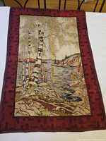 Full view of the large scarf laid flat on a white table showing the detailed nature-inspired design with birch trees and lake scene framed with maroon geometric border.
