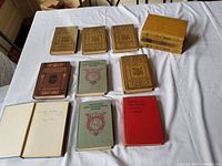 Overview photo showing 12 vintage school books arranged on a white cloth. Various titles and colors of books visible, including brown and green covers, some stacked horizontally.