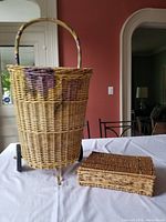 Large decorated wicker shopping basket with wheels and smaller rectangular wicker basket on table