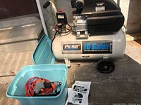 Side and angled view of Pulsar 10 Gallon air compressor with pressure gauge and control knob. Blue plastic container in front holds a red coiled air hose and orange-gray nail gun.