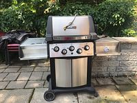 Full front view of Broil King stainless steel barbecue with side shelves, wheels and control knobs on front panel.