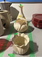 View of three Belleek china pieces including two cache pots and one vase on a table with green tape markers indicating measurements.