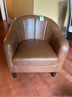 Front view of a brown vinyl club chair with curved back and armrests sitting on a wooden floor.