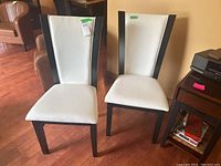 Pair of side chairs, showing front view, white vinyl upholstery, dark wood veneer frame, hardwood flooring background.