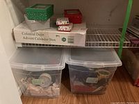 Two plastic totes on a shelf with Christmas decorations and a large advent calendar box labeled Colonial Door Advent Calendar Box