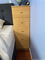 Side view of faux wood five drawer dresser next to bed, showing overall condition and design.