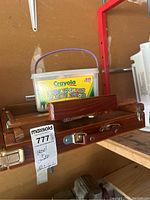 Wooden portable easel folded and stacked with other wooden cases, Crayola chalk crayon plastic container on shelf nearby