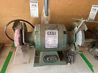 Front view of AIT bench grinder showing wire brush wheel on left and grinding wheel on right with motor label in center.