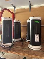 Four white and black Noma tower-style electric space heaters on a wooden surface with cords wrapped around bases, untested condition.