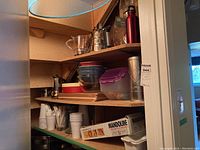View of pantry shelf showing mandoline in original box, stacked glass mixing bowls, plastic containers, and travel mug.
