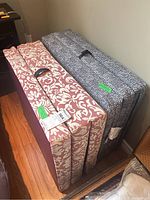 Two folded foam mattresses stacked side by side, showing patterned exteriors and carrying handles.