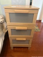 Front view of laminate nightstand showing 3 drawers with plastic inset fronts and wooden handles.