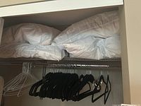 White pillows stacked on upper closet shelf with various black and white hangers below on closet rod.